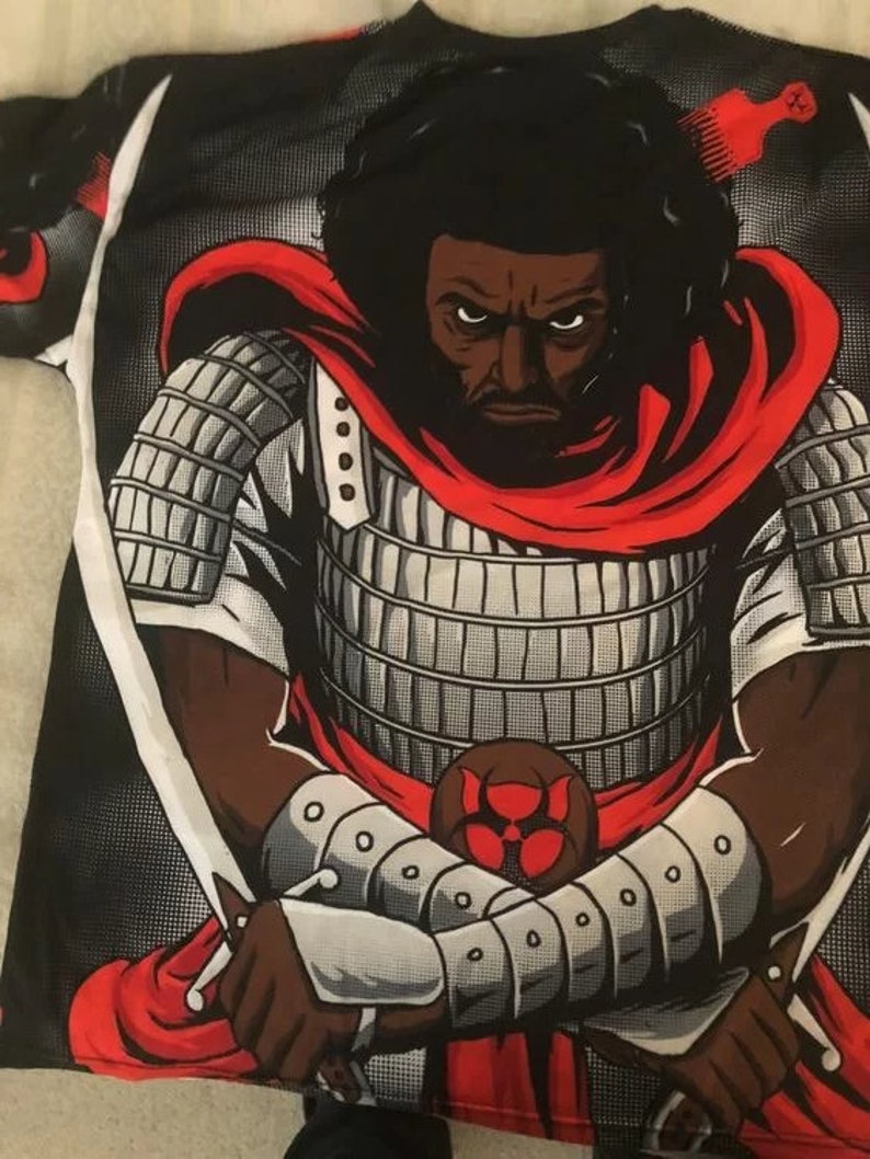 Puede incluir: Una camiseta negra y roja con un estampado gr&aacute;fico de un guerrero samur&aacute;i negro que lleva una capa roja y sostiene dos espadas. El guerrero tiene un afro negro y una expresi&oacute;n seria.