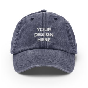 May include: A dark blue denim baseball cap with the text "YOUR DESIGN HERE" embroidered in white on the front.