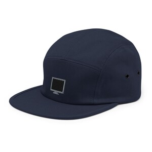 Puede incluir: Una gorra de 5 paneles azul marino con un gráfico de pantalla de ordenador negro bordado en la parte delantera.