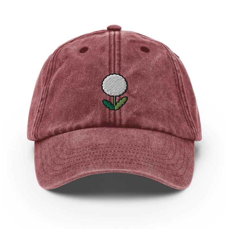 May include: A maroon vintage-style baseball cap with an embroidered white dandelion design.