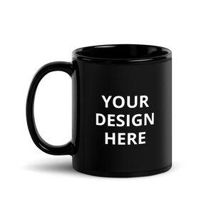 Può includere: Una tazza in ceramica nera con un manico curvo. La tazza presenta il testo bianco "YOUR DESIGN HERE" in un carattere grassetto senza grazie. La tazza è progettata per design personalizzati.