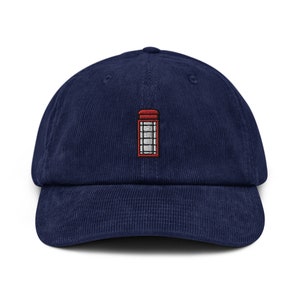 May include: A navy blue corduroy baseball cap with an embroidered red telephone booth design.