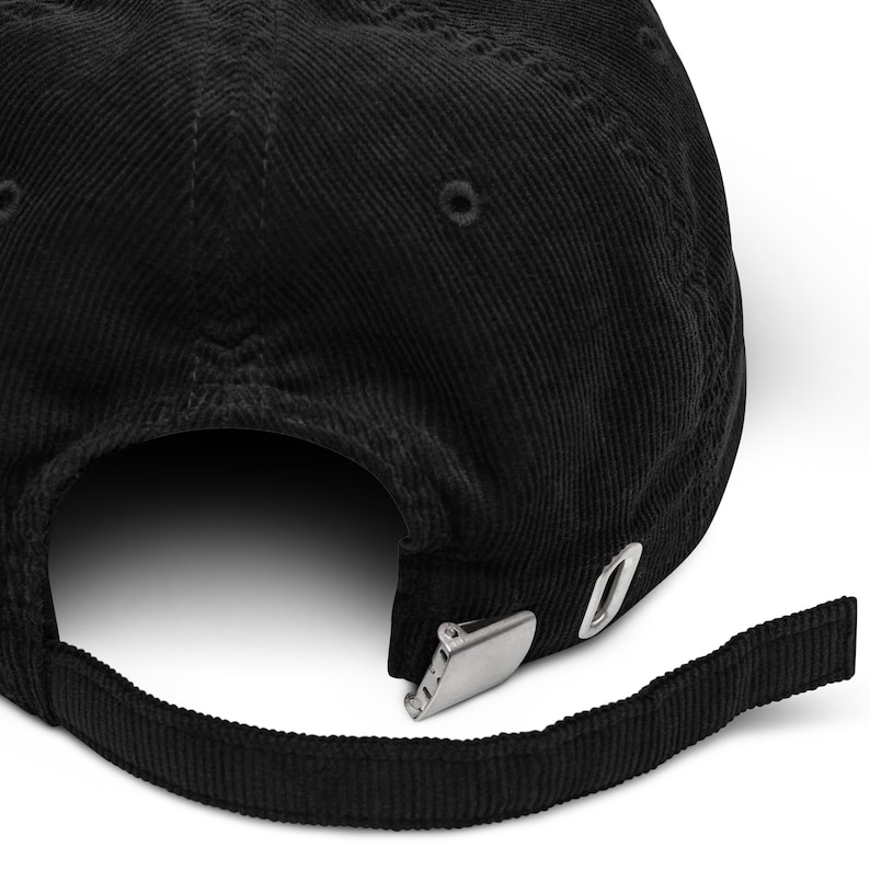 May include: Black corduroy baseball cap with an adjustable strap and a metal buckle closure.