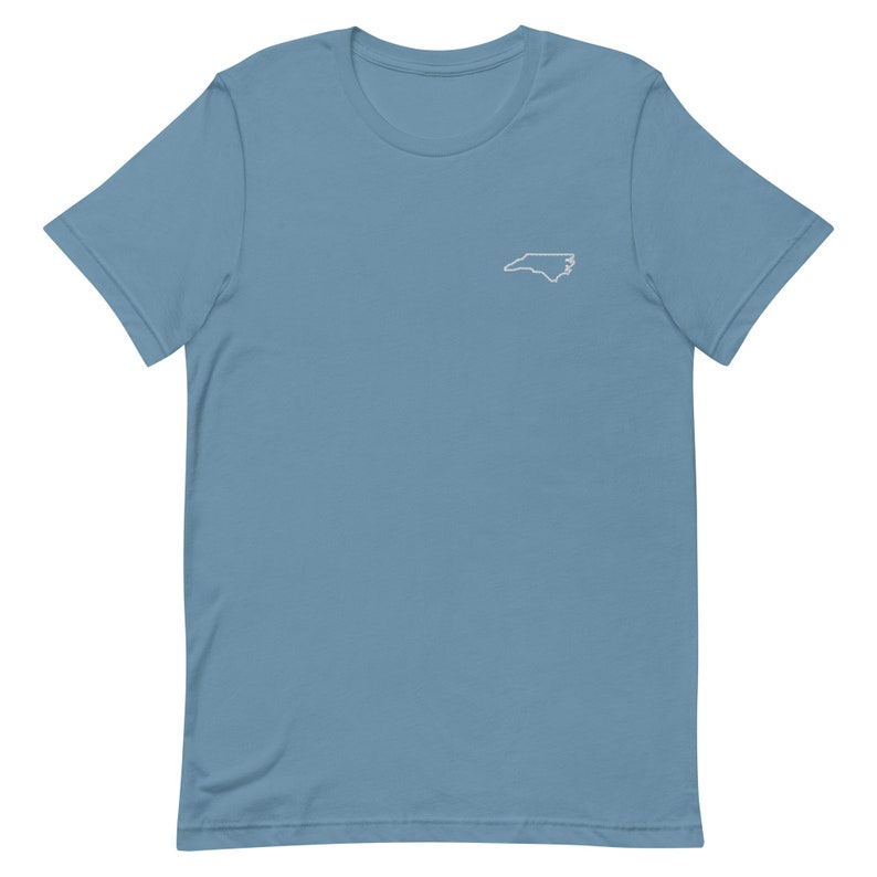 Puede incluir: Una camiseta azul claro con un contorno blanco del estado de Carolina del Norte en la parte delantera.