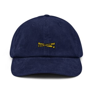 Op de afbeelding: Marineblauwe corduroy baseballcap met een gebogen klep. De pet heeft een geborduurd geel "DO NOT CROSS" waarschuwingslint ontwerp op de voorkant. De hoed heeft een gestructureerde pasvorm en een klassiek zes-panelen ontwerp.