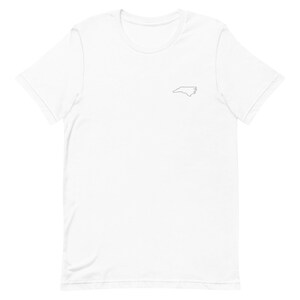 Puede incluir: Camiseta blanca con un peque&ntilde;o contorno del estado de Carolina del Norte en el pecho izquierdo.