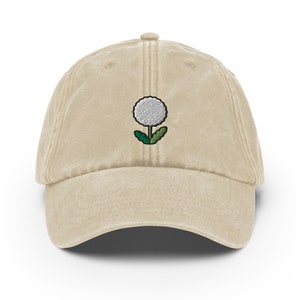 May include: A beige cotton baseball cap with an embroidered white dandelion design.