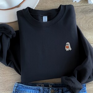 May include: Black sweatshirt with a small embroidered ghost holding a book. The ghost is white with a light orange book.