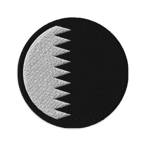 Puede incluir: Un parche redondo bordado en blanco y negro con una luna creciente blanca y bordes dentados sobre un fondo negro.