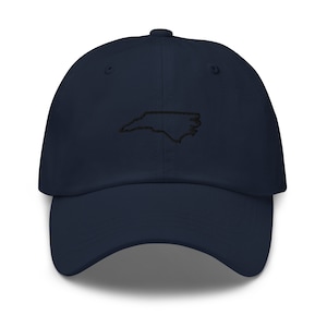 K&ouml;nnte beinhalten: Eine marineblaue Baseballkappe mit einer gestickten Umrandung des Bundesstaates North Carolina in Schwarz.
