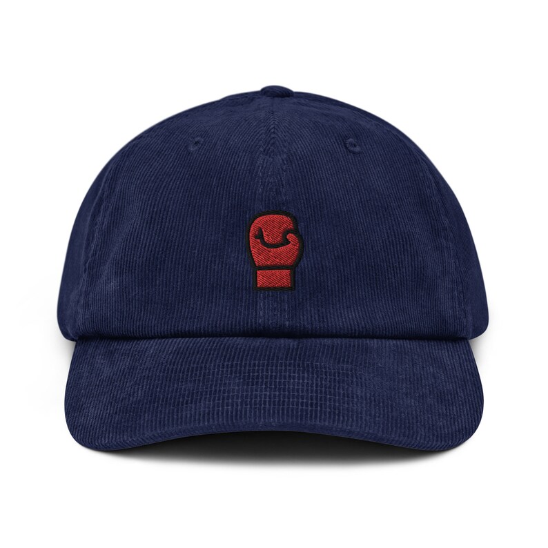 May include: A navy blue corduroy baseball cap with a red embroidered boxing glove on the front.