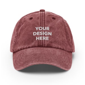 May include: A maroon vintage-style baseball cap with a white embroidered design that says "YOUR DESIGN HERE".