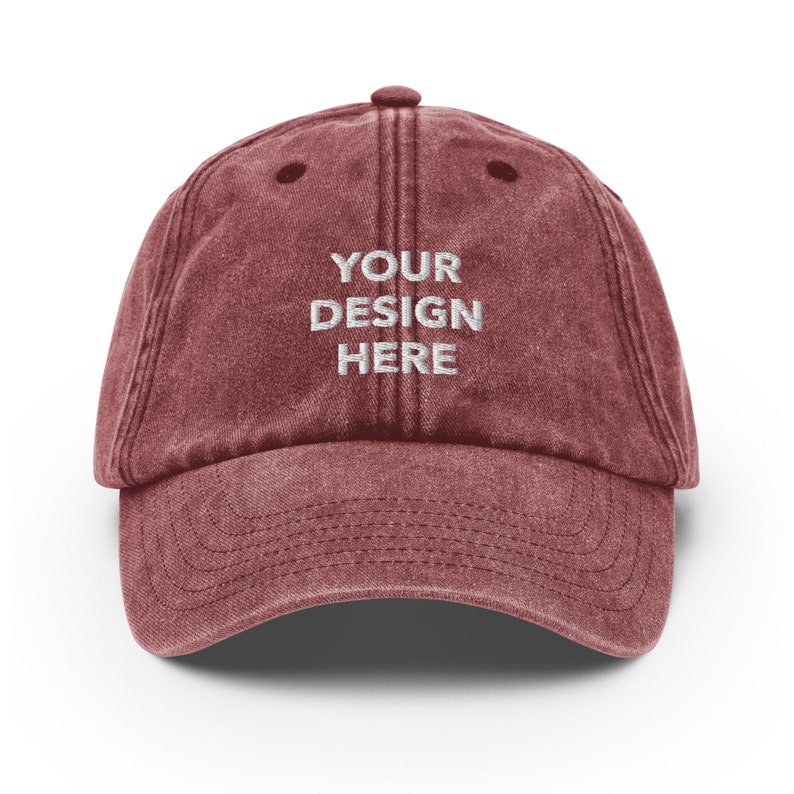 May include: A maroon vintage-style baseball cap with a white embroidered design that says "YOUR DESIGN HERE".