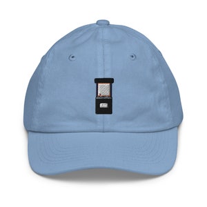 May include: A light blue baseball cap with an embroidered arcade game on the front. The arcade game is black with a white screen and red and orange lights.