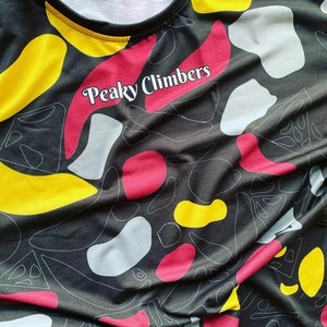 Puede incluir: Camiseta de tirantes negra con un patr&oacute;n abstracto de colores y el texto "Peaky Climbers" impreso en la parte delantera.