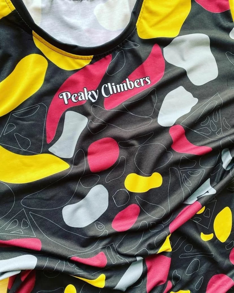 Puede incluir: Camiseta de tirantes negra con un patr&oacute;n abstracto de colores y el texto "Peaky Climbers" impreso en la parte delantera.
