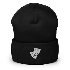 Peut inclure: Un bonnet noir avec un motif brodé blanc de deux masques de théâtre, l'un souriant et l'autre fronçant les sourcils.