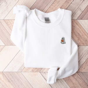 May include: White sweatshirt with a small embroidered design of a ghost reading a book.