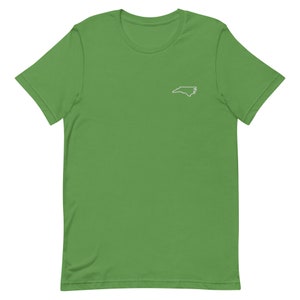 Puede incluir: Una camiseta verde de manga corta con un contorno blanco del estado de Carolina del Norte en el pecho izquierdo.