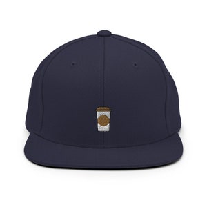 Puede incluir: Una gorra de béisbol azul marino con un diseño de taza de café bordada en blanco y marrón.