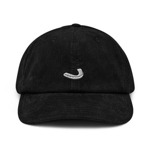 Puede incluir: Gorra de béisbol de pana negra con un diseño blanco bordado curvo en la parte delantera. La gorra tiene una corona estructurada y una visera curva. El sombrero es de color negro liso.
