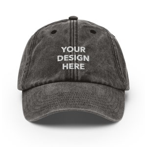 May include: A black distressed baseball cap with the text "YOUR DESIGN HERE" embroidered in white on the front.