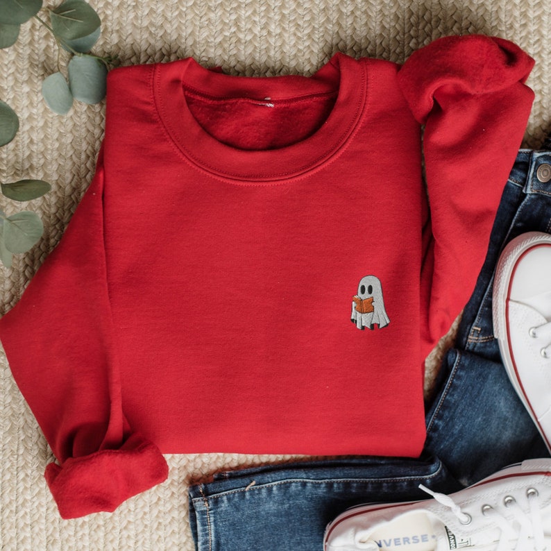 May include: Red sweatshirt with a small embroidered ghost reading a book. The ghost is white with a gray face and a light orange book.