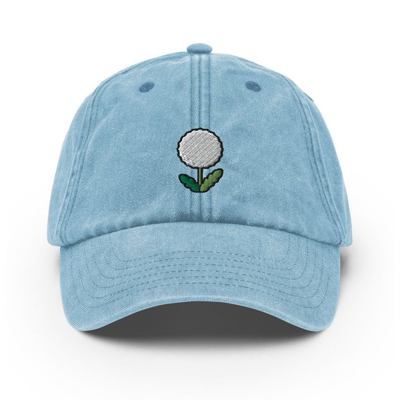 May include: A light blue denim baseball cap with an embroidered white dandelion design.
