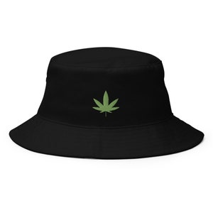 Op de afbeelding: Een zwarte bucket hat met een groen marihuanablad geborduurd op de voorkant.