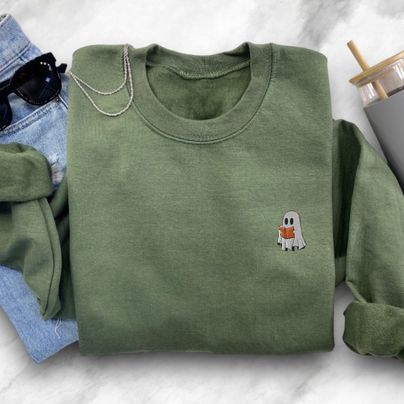 May include: A green sweatshirt with a small embroidered ghost reading a book. The ghost is white with a red book.