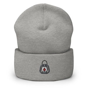 Puede incluir: Gorro gris con una pequeña imagen bordada de una linterna con una llama roja.