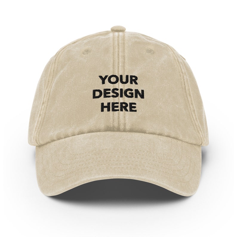 May include: A beige cotton baseball cap with the text "YOUR DESIGN HERE" embroidered in black on the front.