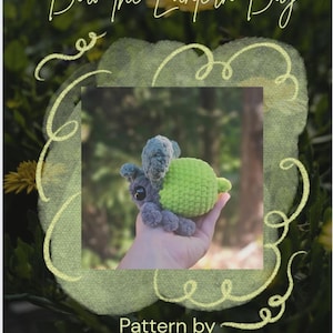 May include: A handmade crochet bug with a green body and blue-grey wings is held in a hand. The bug is a whimsical design, with the text "Bow the Lantern Bug" at the top. The bottom of the image reads "Pattern by @mommachase_crafts".