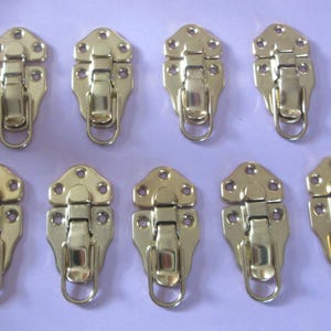 May include: Ten gold-toned metal clasps with a hook and latch design. The clasps are all identical and have a decorative, ornate design.