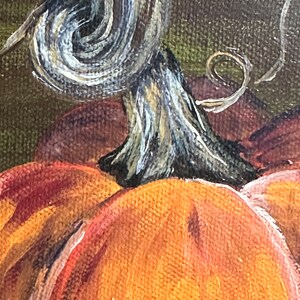 May include: Close-up of a painted orange pumpkin with a brown stem. The stem is curled and has a light gray and brown swirl pattern.