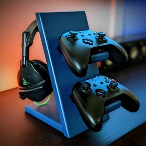 May include: A blue stand with two black video game controllers and a black headset. The stand is on a dark brown surface.