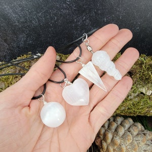 May include: Four selenite crystal pendants on black cords. The pendants are a sphere, a heart, a point, and a long, thin, rounded shape.