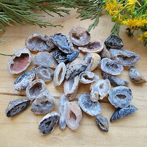 Puede incluir: Una colección de geodas de cristal de ágata natural en varias formas y tamaños. Las geodas son una mezcla de colores grises, blancos y marrones con una textura natural y rugosa.