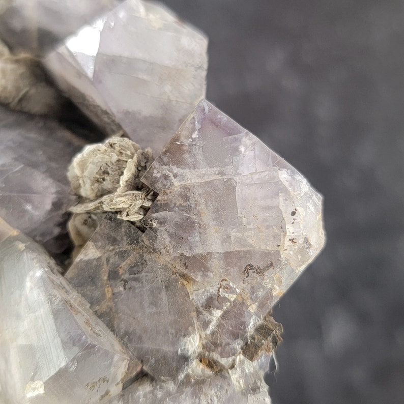 Op de afbeelding: Een cluster van paarse fluorietkristallen met een ruwe, natuurlijke textuur. De kristallen zijn doorschijnend en hebben een lichte glans.