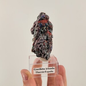 Könnte beinhalten: Ein kleines, irisierendes Goethit-Exemplar aus Tharsis, Spanien. Das Mineral hat eine geschichtete, strukturierte Oberfläche in Rot-, Lila- und Silbertönen.