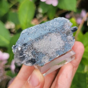 May include: A raw mineral specimen featuring a cluster of dark blue, crystalline formations with a textured, sparkling surface. The mineral is mounted on a clear, rectangular acrylic base, showcasing its natural, jagged edges and deep blue hues.
