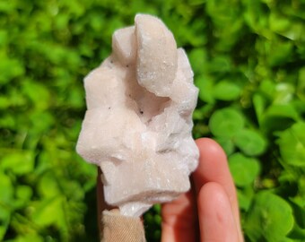May include: A cluster of pink selenite crystals with a rough, natural texture. The crystals are clustered together in a unique formation, creating a visually interesting piece.