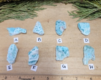 May include: Nine different pieces of blue and green ocean jasper, labeled A through I, on a wooden surface. The pieces are all different shapes and sizes.