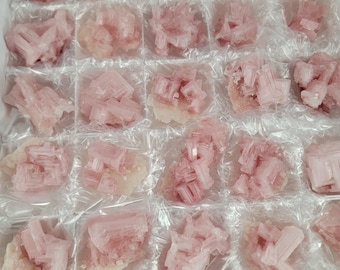 Op de afbeelding: Een verzameling roze kristalclusters, elk afzonderlijk verpakt in helder plastic. De kristallen hebben een zacht, doorschijnend uiterlijk en zijn gerangschikt in een rasterpatroon, wat wijst op een mineraalmonsterdisplay.