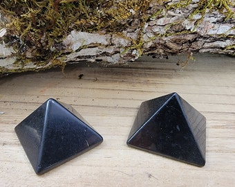 May include: Two black obsidian pyramids on a wooden surface. The pyramids are smooth and polished.