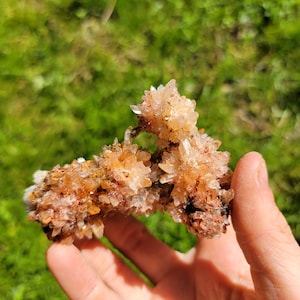 May include: A cluster of small, delicate, light pink and white crystals with a rough, brown base. The crystals are clustered together in a natural formation, creating a unique and interesting piece.