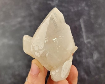 Op de afbeelding: Een helder kwartskristal met een unieke, gefacetteerde vorm. Het kristal heeft een melkachtig witte kleur en is doorschijnend.