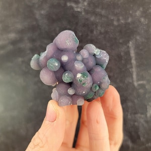 May include: A cluster of botryoidal chalcedony, featuring rounded, grape-like formations. The stone displays a soft lavender hue with patches of green and white. The overall shape is irregular, with a smooth, polished appearance. This natural specimen is a unique decorative item.