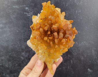 May include: A cluster of orange and clear quartz crystals, with a pointed shape, resembling a flower.