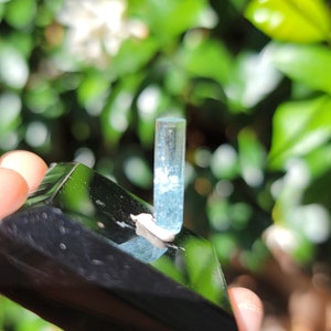以下が含まれることがあります： 透明でファセットカットされた半透明の薄い青色のアクアマリンの結晶。結晶は黒い表面に置かれています。